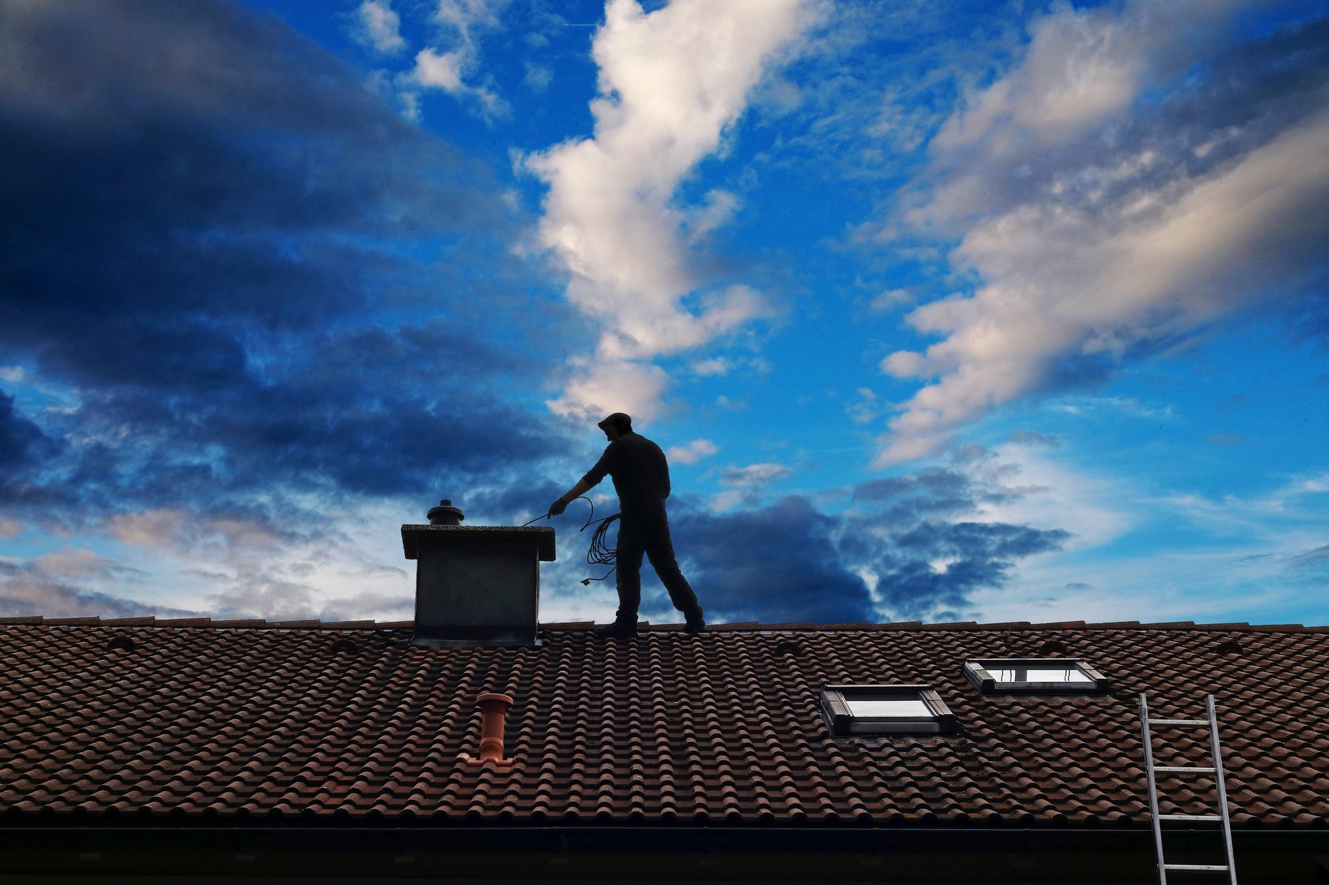 Kaminfeger bei der Arbeit auf einem Dach mit dramatischem Himmel