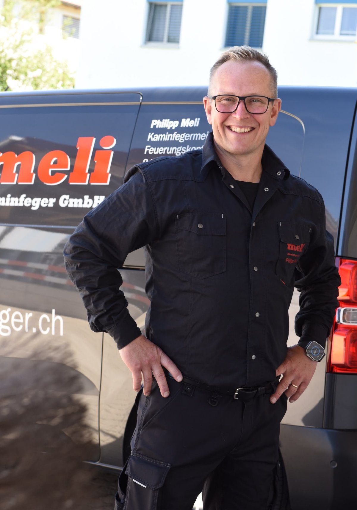 Mann in schwarzer Arbeitsjacke mit Brille vor blauem Service-Fahrzeug