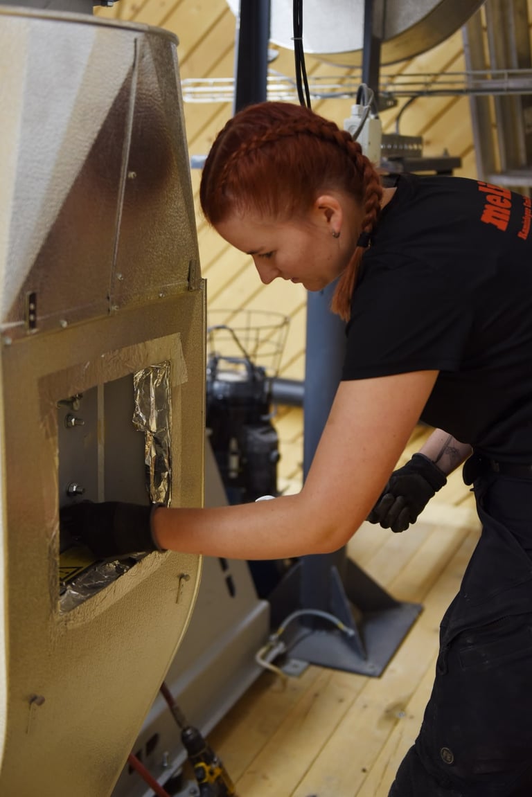 Frau in schwarzem Shirt mit Arbeitshandschuhen bedient gelbe Industriemaschine in Werkstatt