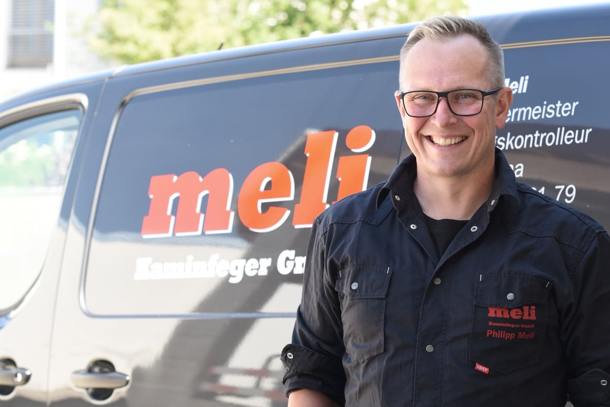 Mann mit Brille in schwarzer Meli-Jacke lächelt vor grauem Arbeitsfahrzeug mit Meli-Branding