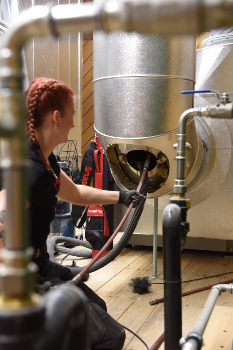 Frau mit rot geflochtenen Haaren bedient ein grosses industrielles Gärgefäss in einer Brauerei